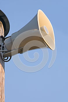 Grey horn loudspeaker on the pole over blue sky