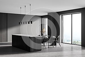 Grey kitchen interior with cutting table and chairs near window, concrete floor