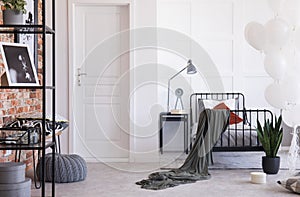 Grey lamp, clock and books on black nightstand next to comfy bed with grey bedding and crimson and white pillows