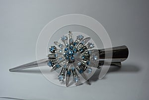 Grey metal hair clip with large metal flower made of blue stones set on white background.