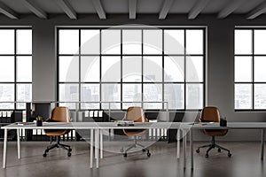 Grey office interior with shared table and chairs in row, shelf and panoramic window