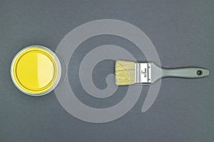 Grey paintbrush with natural bristle and can of yellow paint for house renovation works