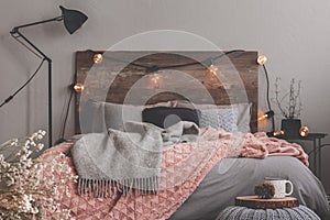 Grey and pastel pink blanket on grey bedding of fashionable bedroom with rustic design