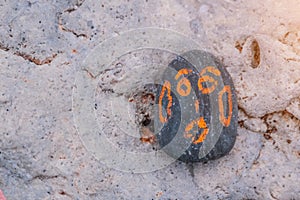 Grey Pebble with a orange painted smiling face. On a small stone is an image of a happy face. Concept: joy, happiness