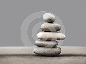 Grey pebbles stacked as a meditation tower or as directional markers on a grey table against a grey wall