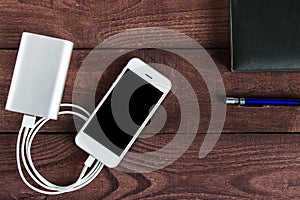 Grey phone and power bank connected by cord with pen and notebook