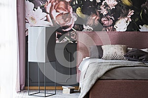 Grey pillows and bedding on bed in pink bedroom interior with flower wallpaper. Real photo
