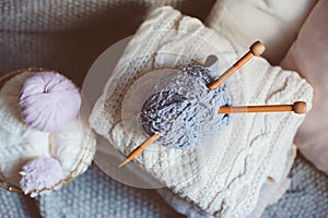 Grey and pink Yarn ball with knitting needles in metallic basket with knitted sweaters on background