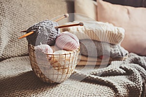 Grey and pink Yarn ball with knitting needles in metallic basket with knitted sweaters on background