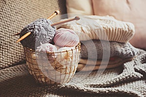 Grey and pink Yarn ball with knitting needles in metallic basket with knitted sweaters on background