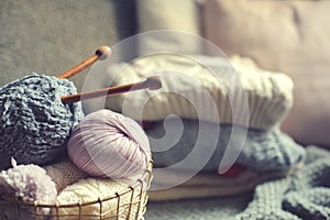 Grey and pink Yarn ball with knitting needles in metallic basket with knitted sweaters on background