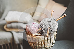 Grey and pink Yarn ball with knitting needles in metallic basket with knitted sweaters on background