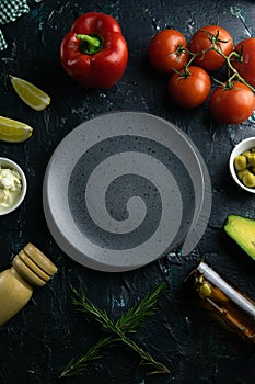 Grey plate with clear space on a black background, around the tomato, souce, olives, lemon, olive oil with spice