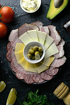 Grey plate with olives around the salami, ham, cheese and mozzarella. Tomato, souce, olives, lemon, olive oil with spice