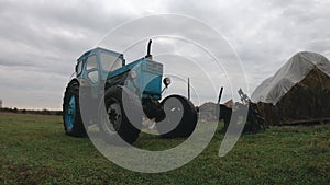 Grey rainy clouds over a vintage blue tractor in the countryside. Unprofitable agribusiness