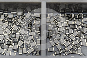 Grey scattered microscopic SMT surface mount chip resistors sorted in grey storage container