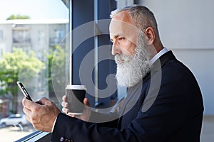 Grey sir age of 50-60 holding cup of coffee and surfing in phone