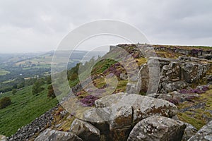 Grey skies over the rock and heather covered slopes of Curbar Edge, Derbyshire, in summer