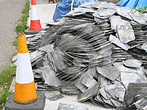 Grey slate shingles for covering a house roof are lying between two traffic cones in Mousehole Cornwall England