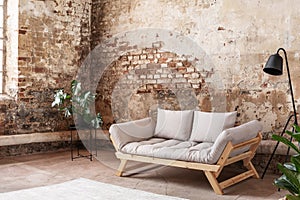 Grey sofa between plant and black lamp in wabi sabi loft interior with red brick wall photo