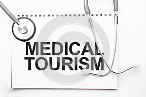 Grey stethoscope and paper plate with a sheet of white paper with text Medical Tourism light blue backround. Medical concept