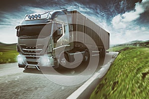 Grey truck moving fast on the road in a natural landscape with cloudy sky