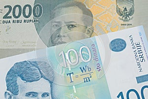 A grey two thousand Indonesian rupiah bank note paired with a bue and white one hundred Serbian dinar note.