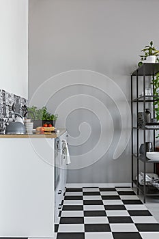 Grey wall in small kitchen with black and white floor and white cupboards