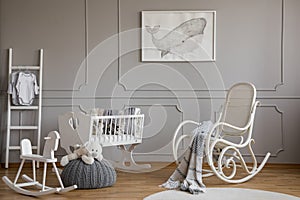 Grey whale on poster in classy baby room interior with white wooden rocking chair, rocking horse, crib and scandinavian ladder,