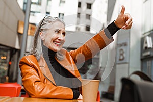 Grey white senior woman gesturing and smiling while sitting in cafe