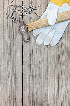 Grey wooden background with old hammer, nails and working gloves