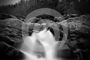 Greyscale Blurred Motion and Slow Shutter Waterscape Photography of a Water Fall over a Large Stones.