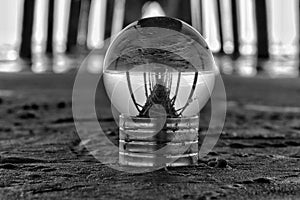 Greyscale of a crystal ball reflecting surface on a beach under a fishing pier