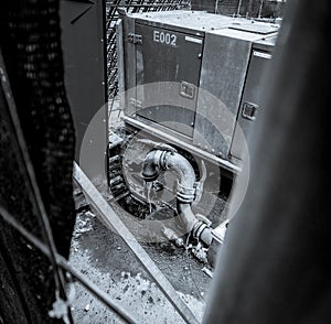 Greyscale image of junkyard, water flowing from industrial pipe