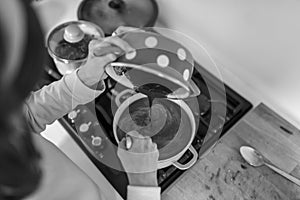 Greyscale image of woman cooking pouring chocolate cream from a