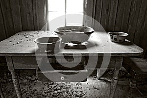Greyscale of an old dusty table with bowls on it in an abandoned building