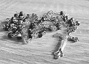 Greyscale photo of a necklace on wooden surface with metallic cross and beads