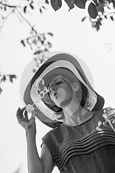 Greyscale portrait of an attractive woman in a wide brimmed sunhat blowing bubbles