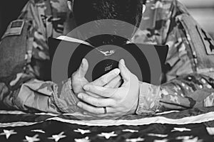 Greyscale shot of an American soldier mourning and praying with the Bible in his hands