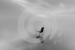 Greyscale shot of a chair on a water surface with a reflection on a rainy day