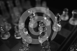 Greyscale shot of glass chess pieces on a wooden chessboard