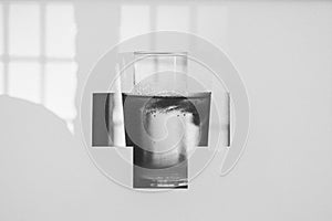 Greyscale shot of liquid medicine in a glass framed with a cross