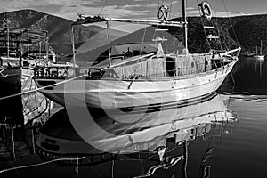 Greyscale shot of a sailing ship in the water with high rocky mountains in the background