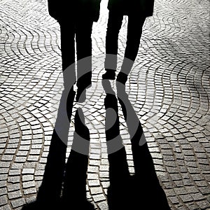 Greyscale shot of the shadows of two people's shadow walking on the street