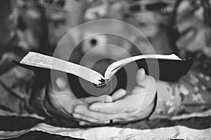 Greyscale shot of a soldier mourning and praying with the Bible and the American flag