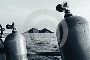 Greyscale of tank cylinders for scuba diving with a sea and an island in the background