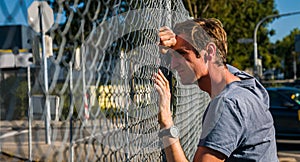 Grieving Man Leaning Head Against Fence