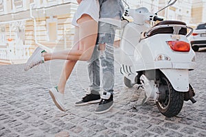 Gril is jumping near guy. Her legs are in air. They are standing beside motorcycle in the middle of street. They have a