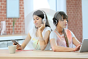 Grilfiends sitting side by side using electronical devices