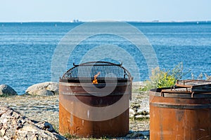 A grill with a charcoal fire burning at a beach location. Blue sky and ocean as a background